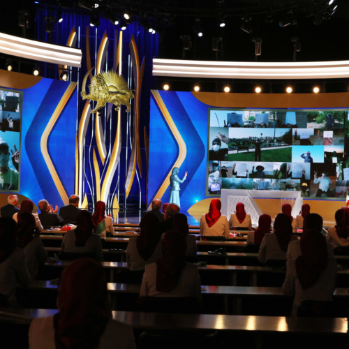 Maryam Rajavi at the Free Iran Global Summit standing in front of collage of Resistance Units in Iran – Ashraf 3, July 17, 2020.